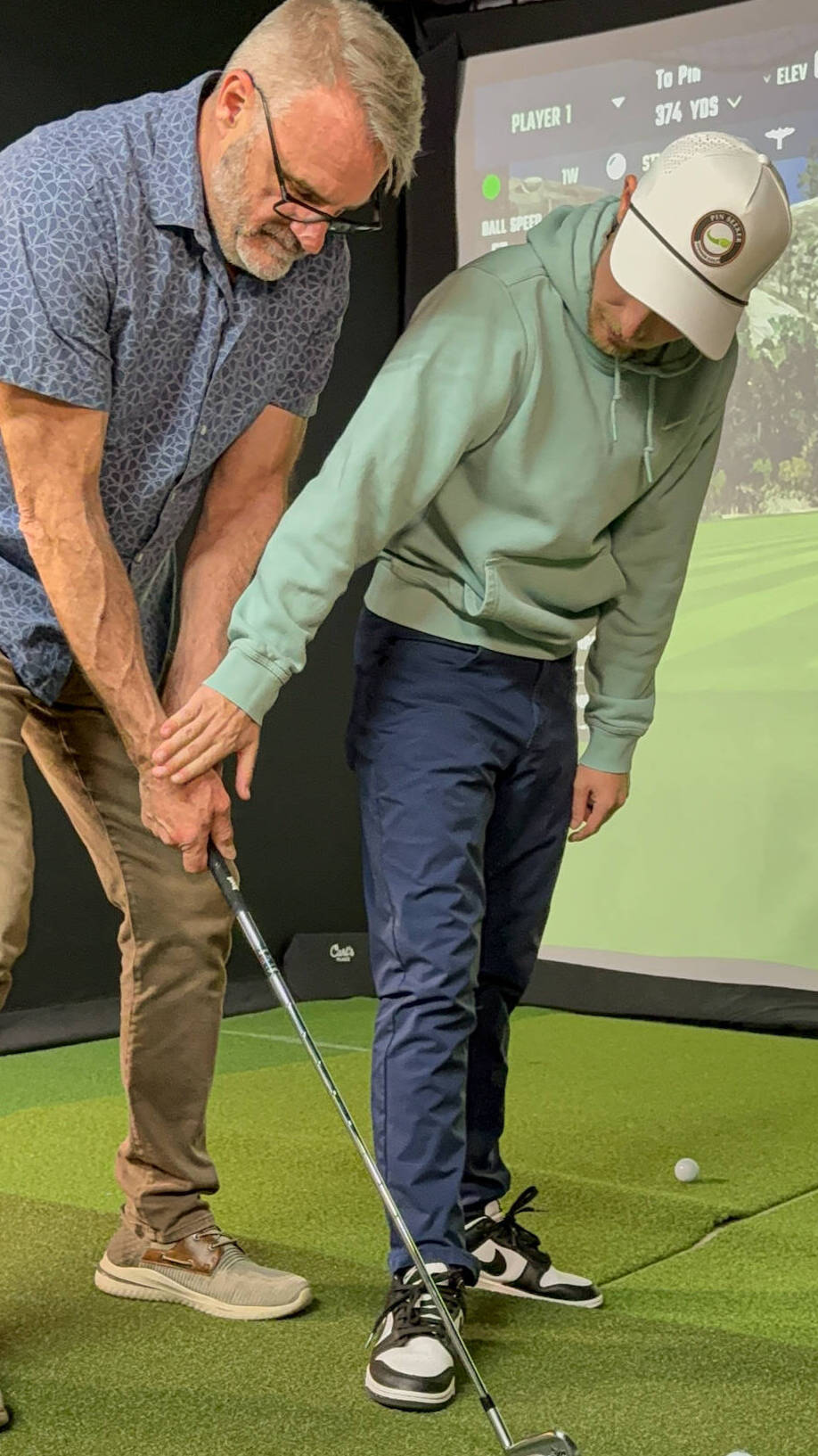 A Pin Seeker instructor adjusting a golfer's grip during a lesson in a simulator bay